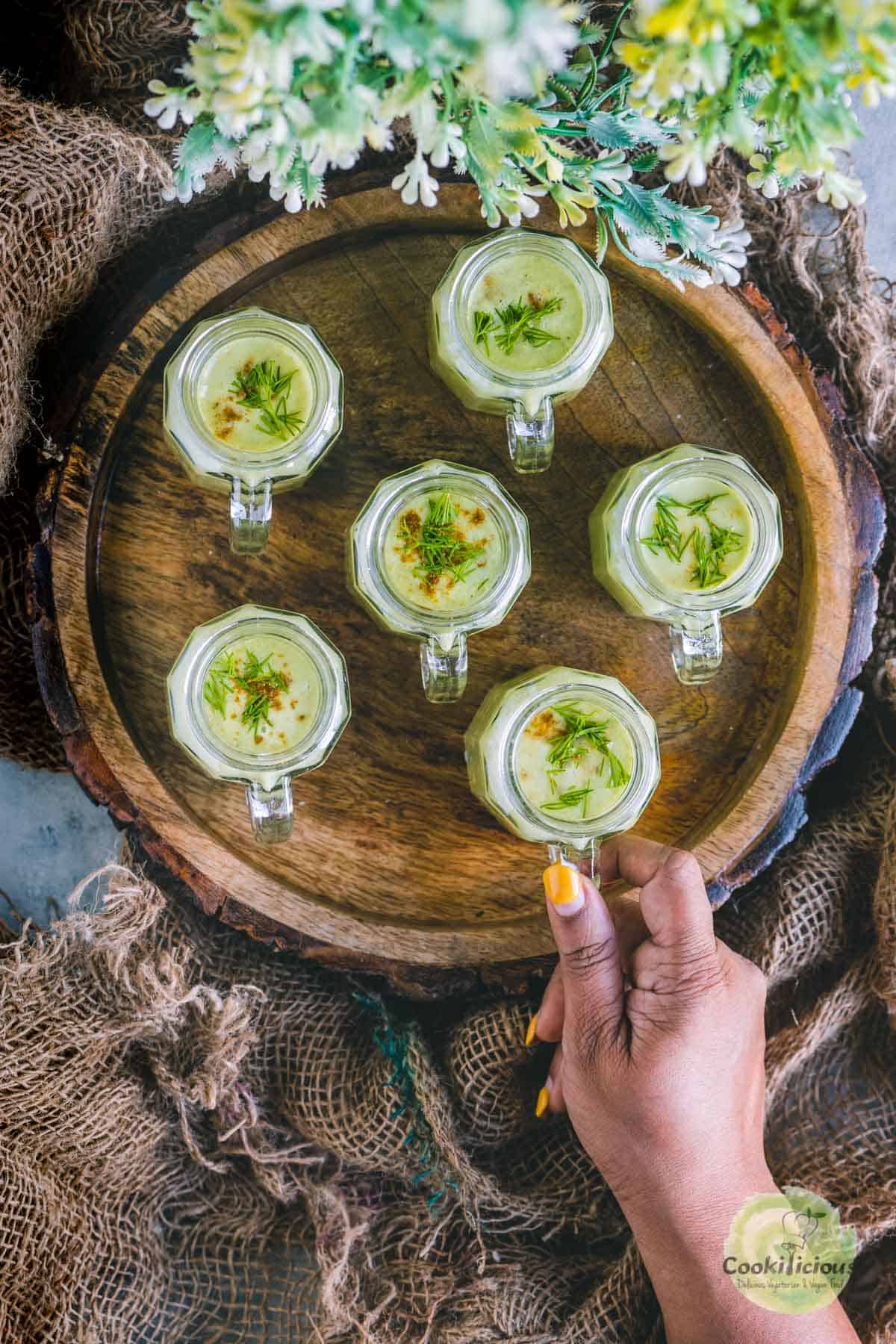 a hand picking up one cucumber soup shot glass from a tray filled the same