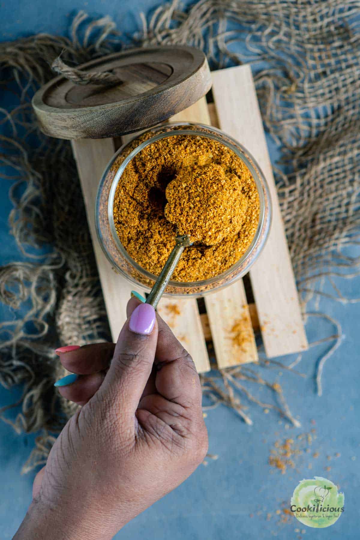 a hand scooping out a spoonful of Sambhar Powder from a jar