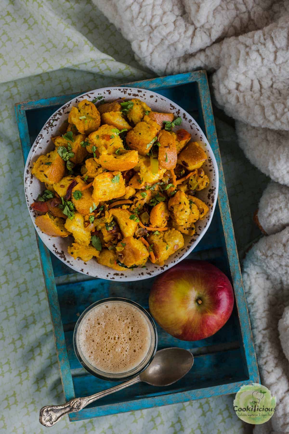 Bread Upma served in a tray with an apple and cup of chai next to it