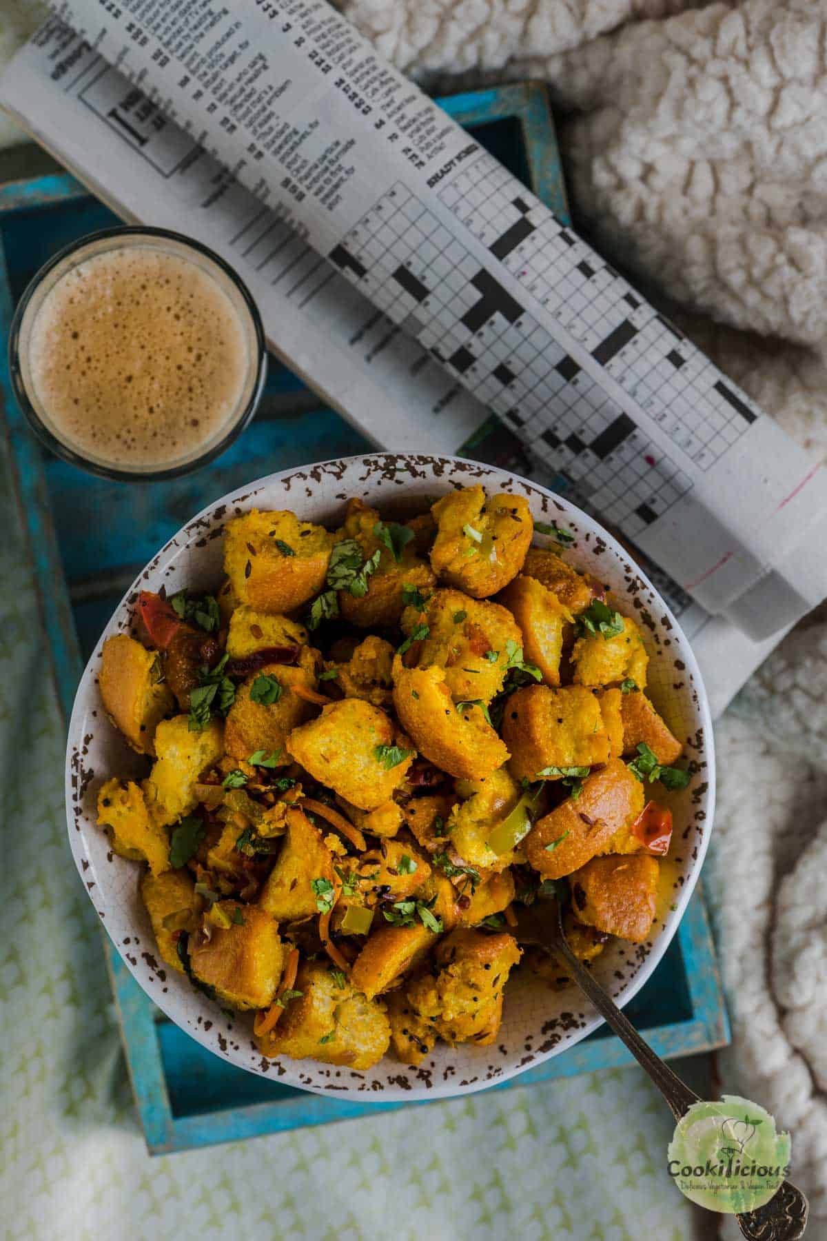 a bowl of Bread Upma served in a tray with chai and newspaper