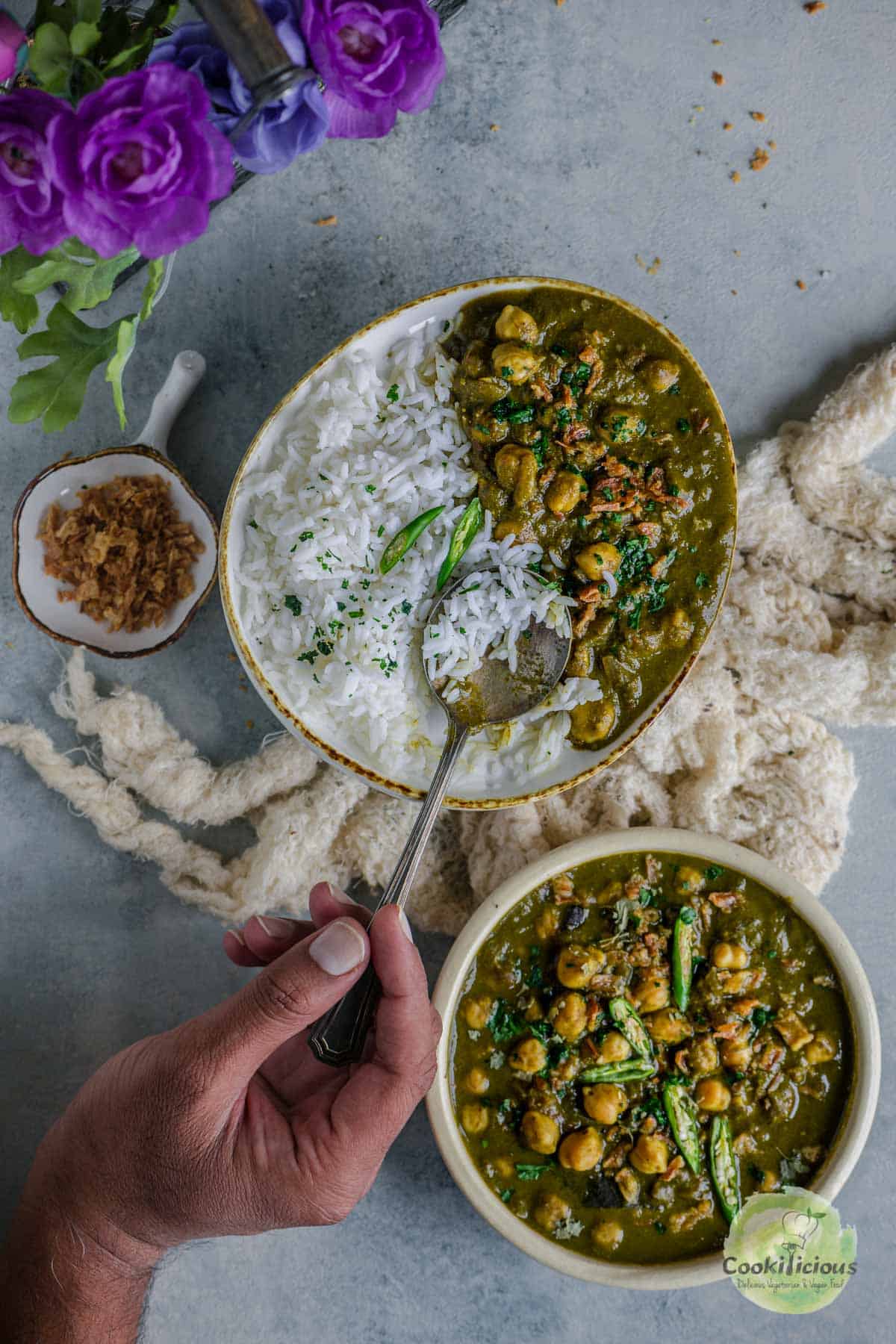 A hand digging into a plate filled with Chickpea Spinach Curry and rice, holding a spoon