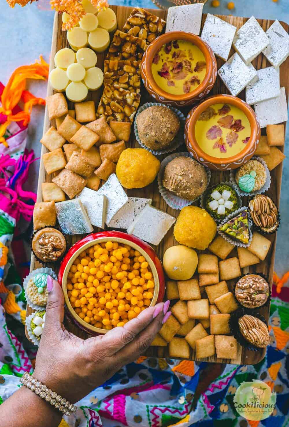 a hand picking up a bowl of boondi from the Indian Dessert Charcuterie Board
