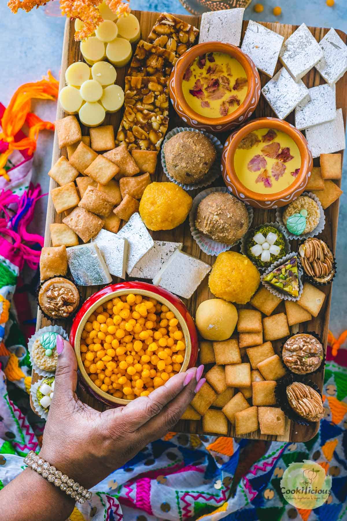 a hand picking up a bowl of boondi from the Indian Dessert Charcuterie Board