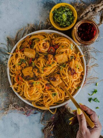 a hand digging into a bowl of spicy Thai noodles with a fork