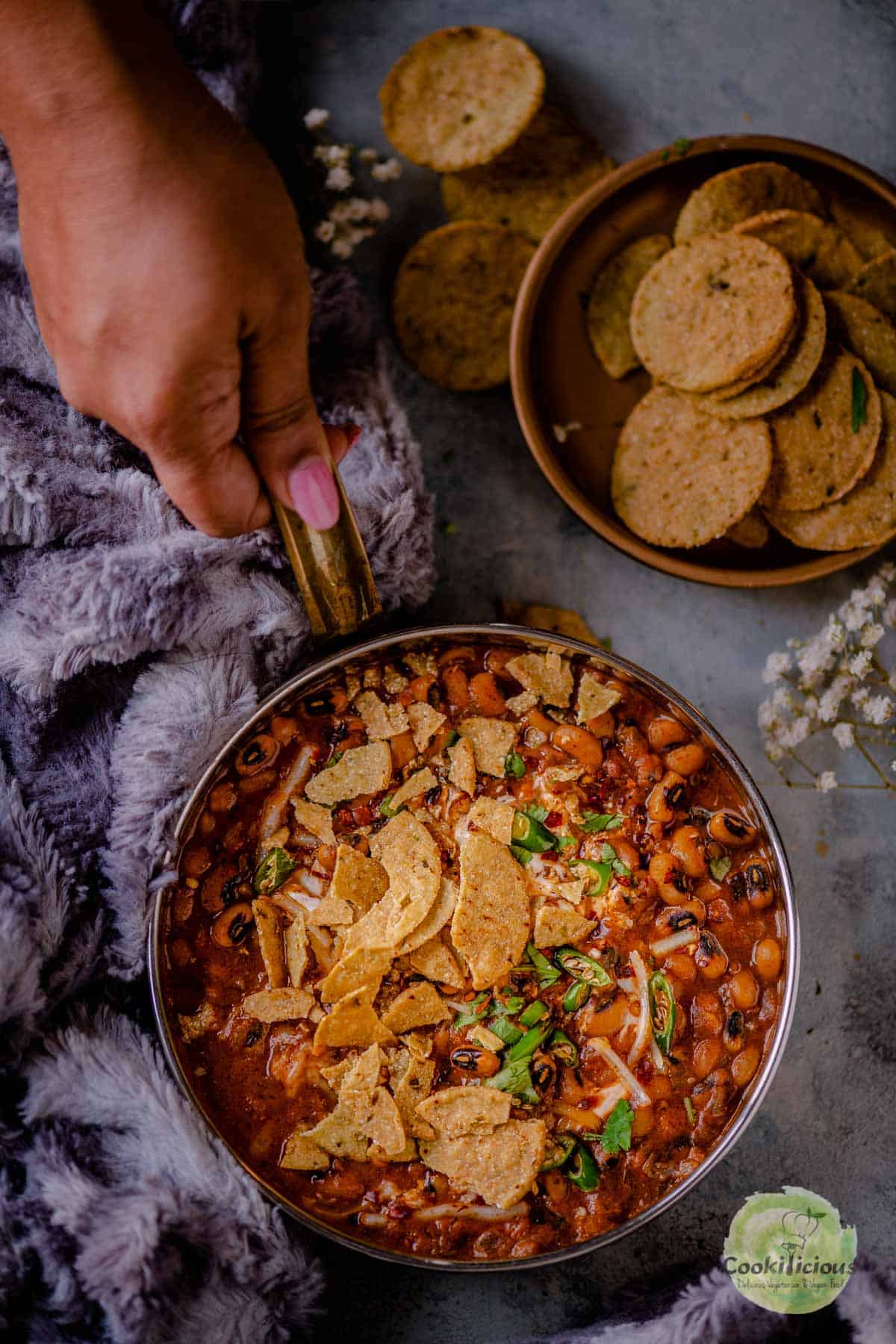 a hand holding a platter filled with Black-Eyed Peas Vegan Chili that's topped with crushed tortilla chips