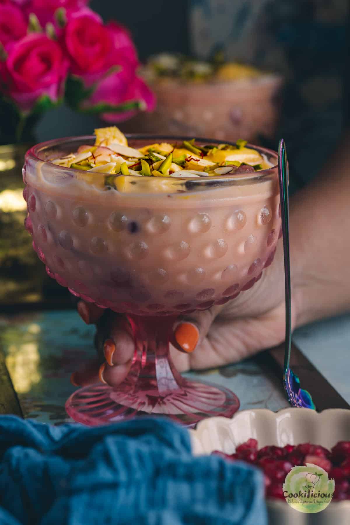 a hand picking up a glass bowl of Indian Fruit Custard