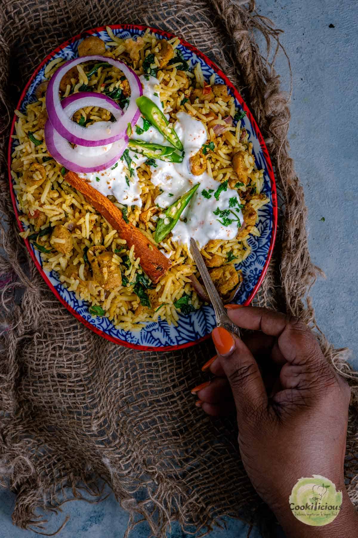 a hand digging into a plate of Soya Chunks Pulao holding a spoon