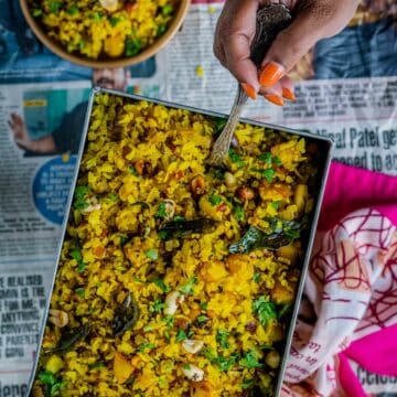 a hand digging into a plate of Kanda Poha holding a spoon
