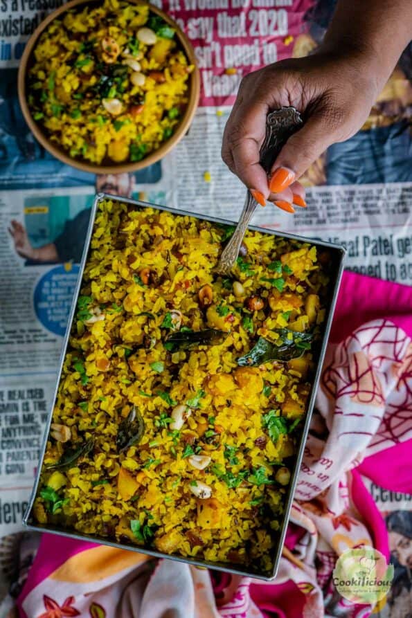 a hand digging into a plate of Kanda Poha holding a spoon