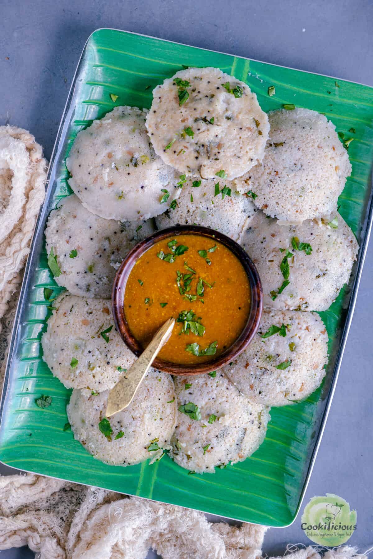 rava oats idli served on a platter with a bowl of sambhar in the center.