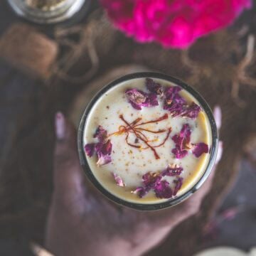 A hand holding a glass of homemade Thandai.