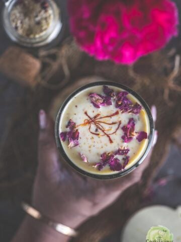 A hand holding a glass of homemade Thandai.