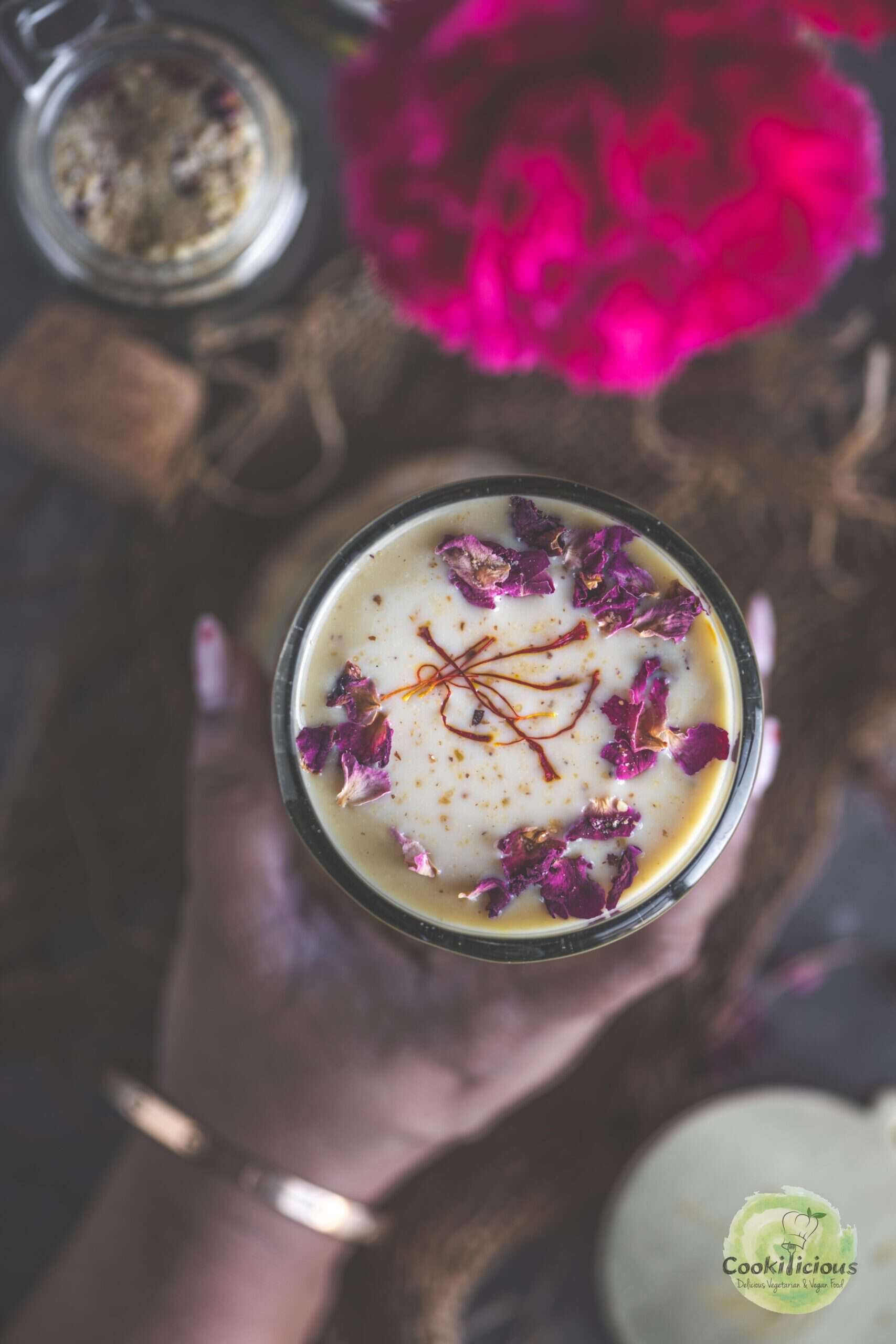 A hand holding a glass of homemade Thandai.