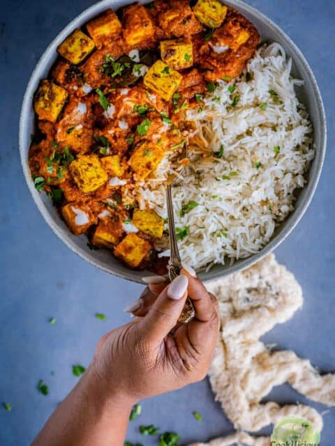 a hand digging into a plate of tofu tikka and rice