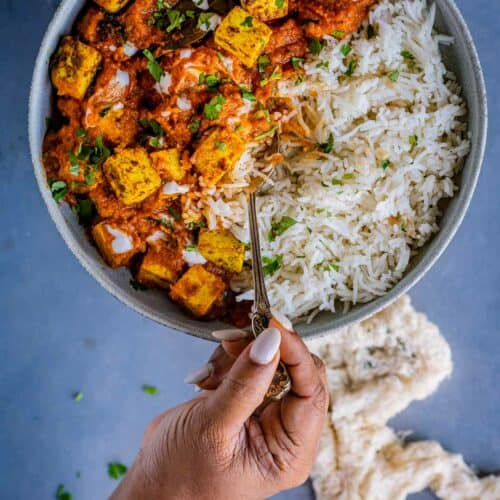 a hand digging into a plate of tofu tikka and rice