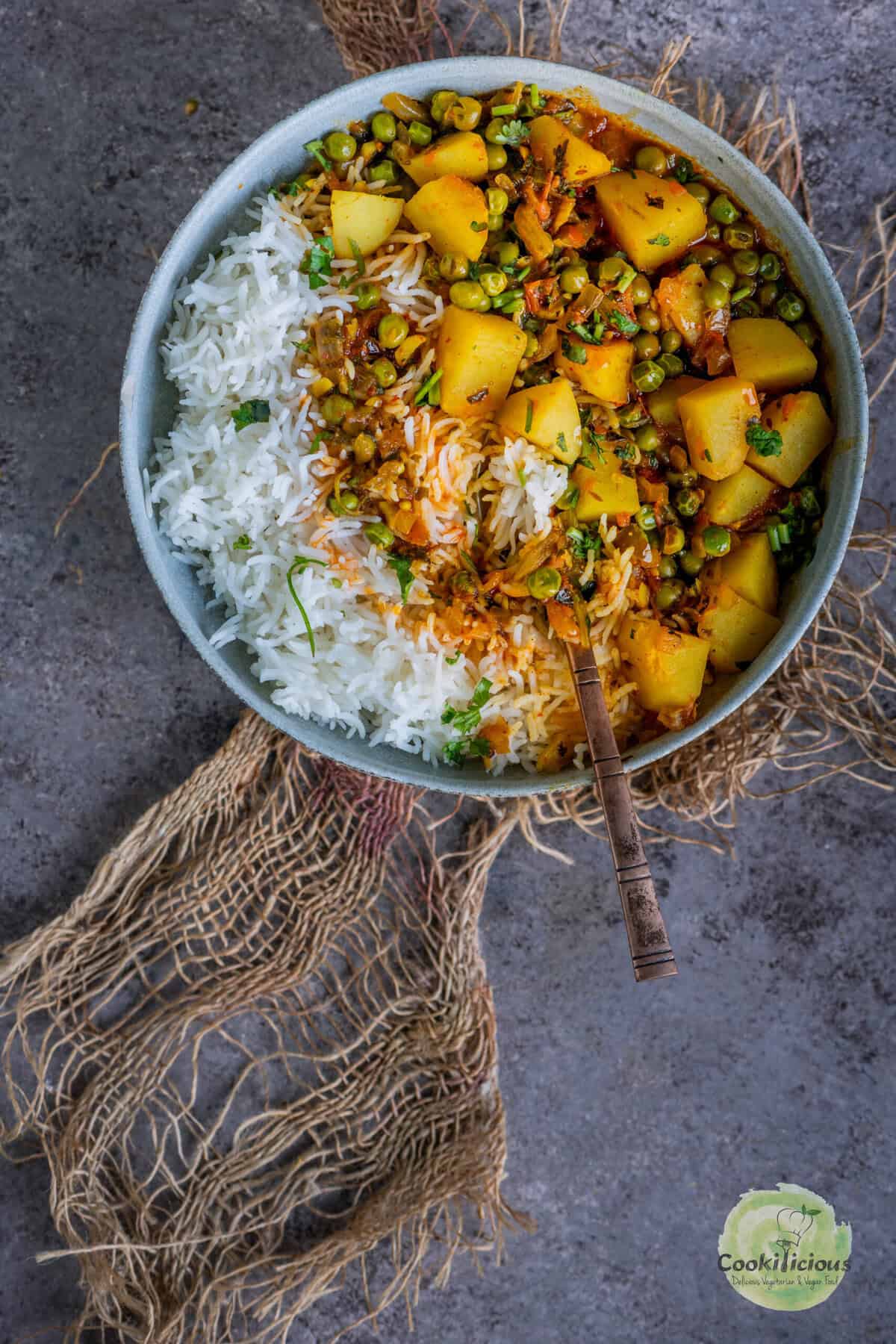 A comforting bowl of Aloo Matar, an Indian potato and green peas curry cooked in a creamy tomato-onion gravy, garnished with fresh cilantro and served with basmati rice.