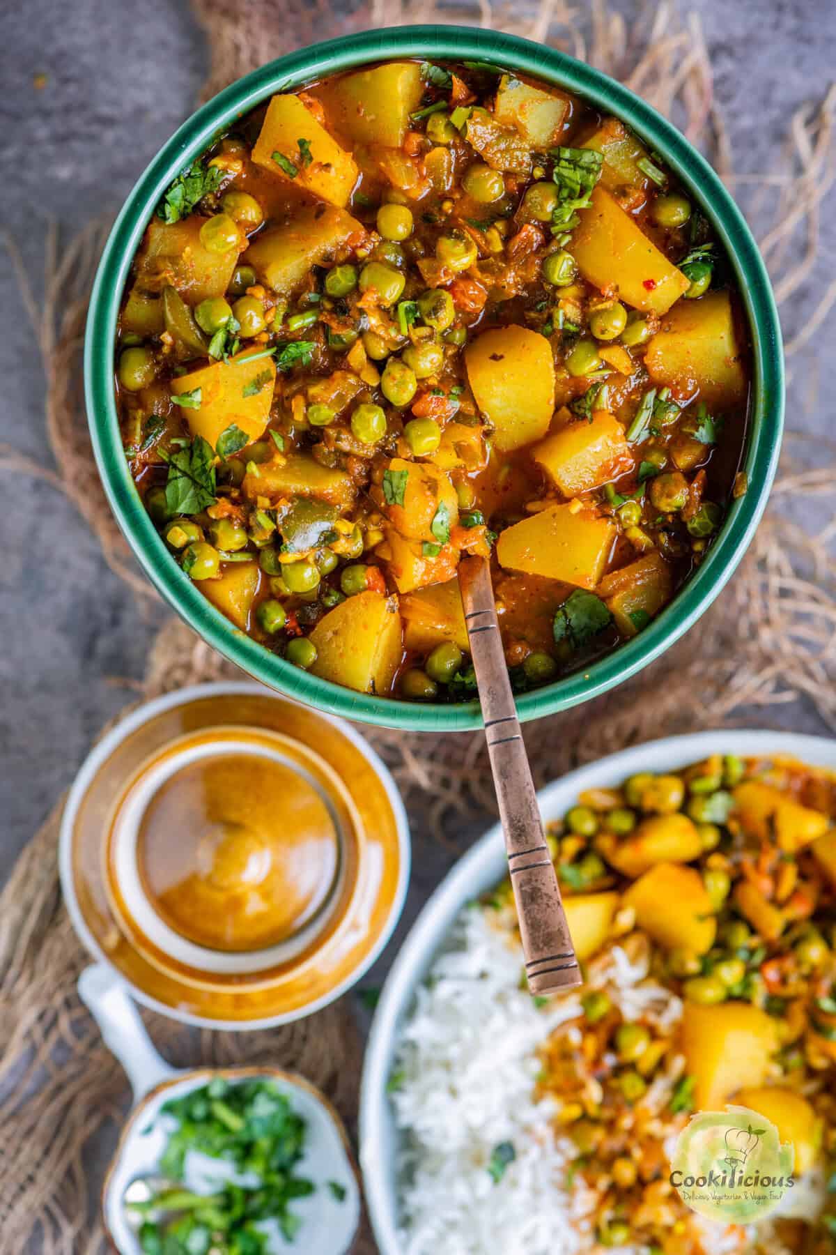 Overhead shot of Aloo Matar curry – tender potatoes and peas simmered in a spiced tomato gravy, served in a bowl with rice on the side.