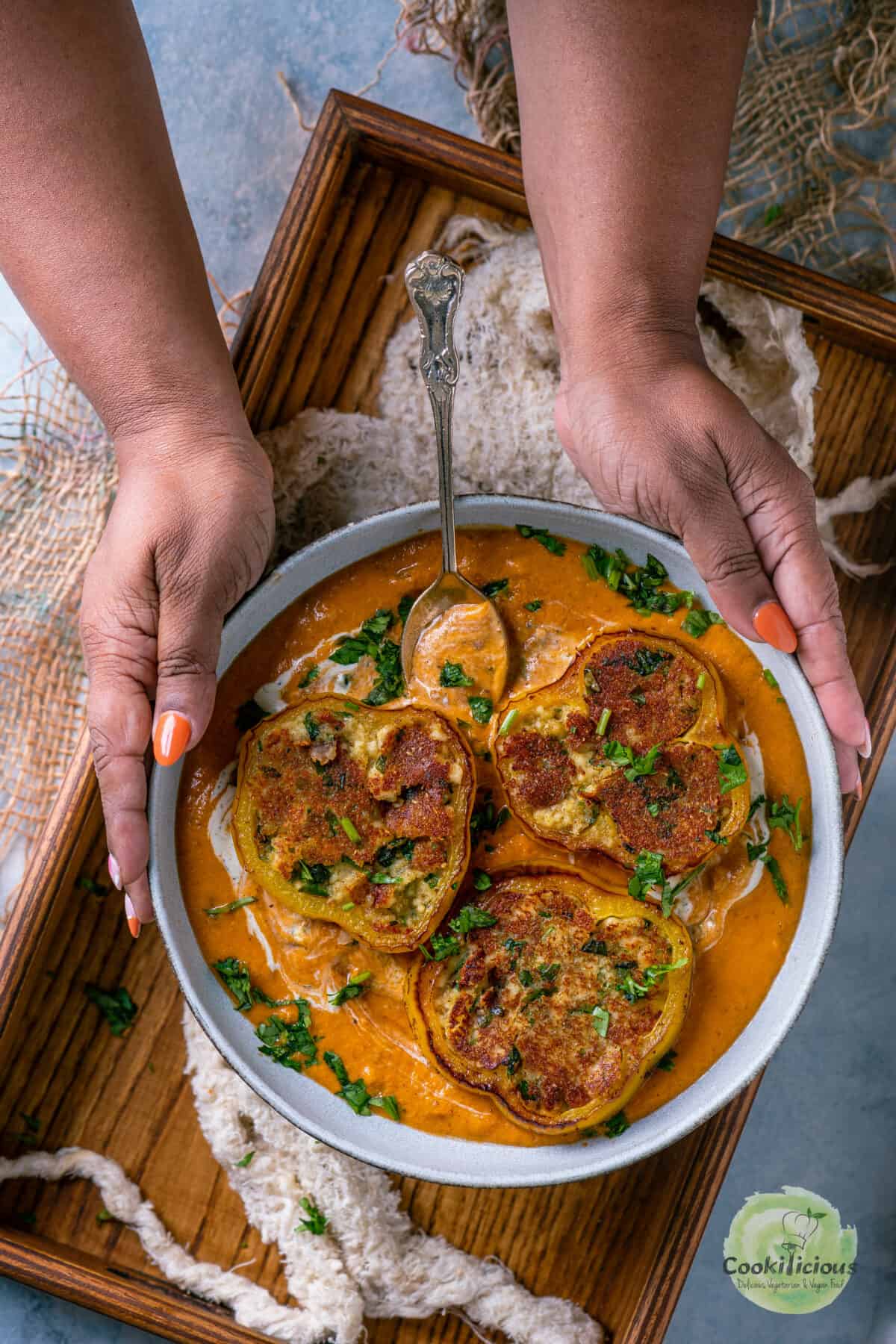 Set of hands holding a bowl of Paneer Masala Stuffed Peppers In Creamy Tomato Gravy.