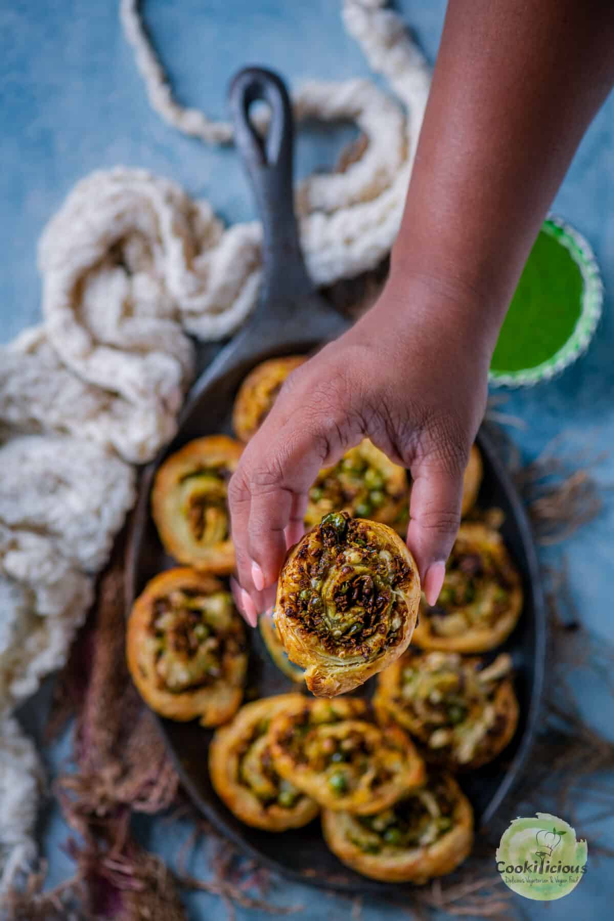 A hand picking up one Puff Pastry Pinwheel With Matar Kachori Filling from a tray.