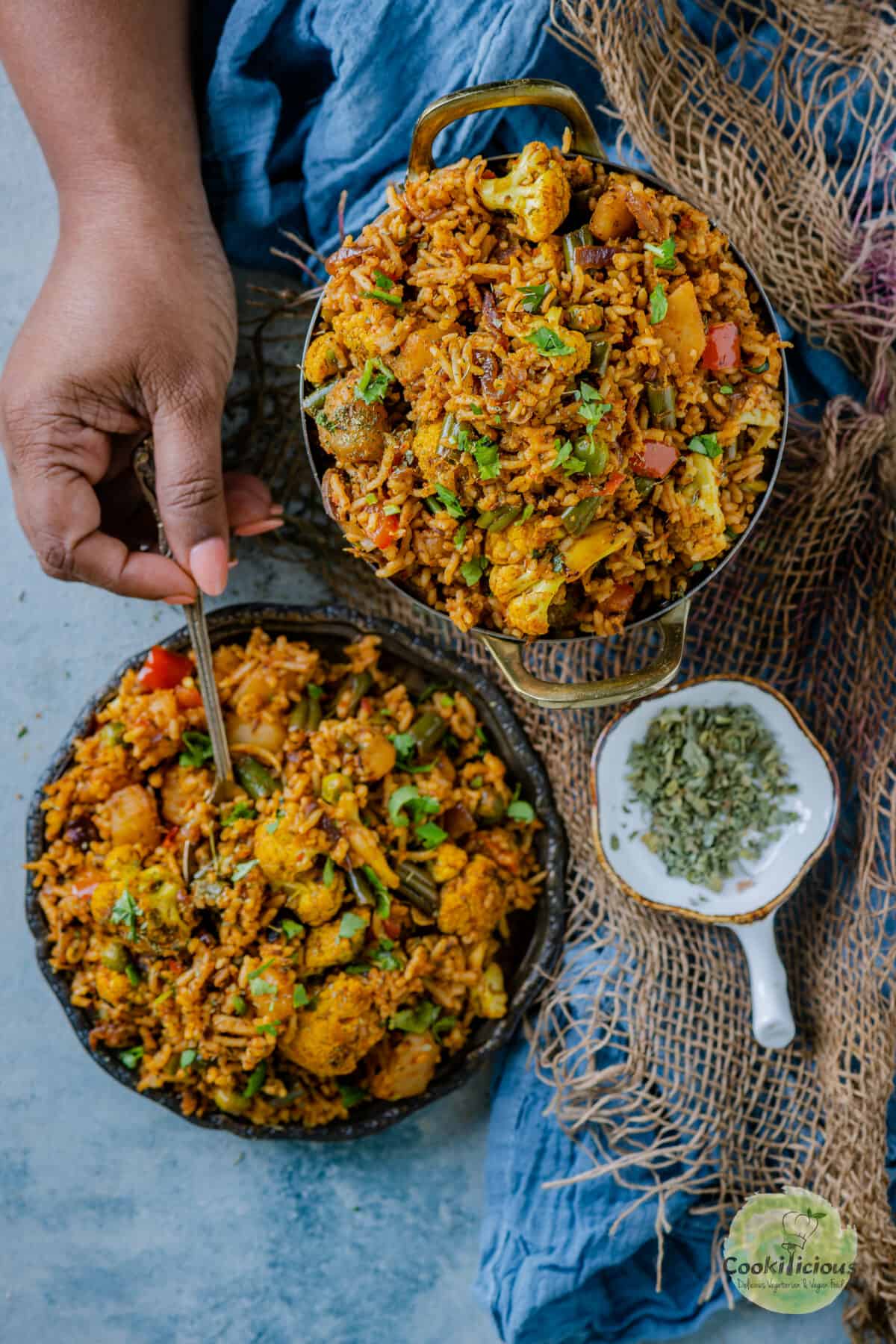 2 bowls of vegan tawa pulao and one hand is digging into one of the bowls with a spoon.