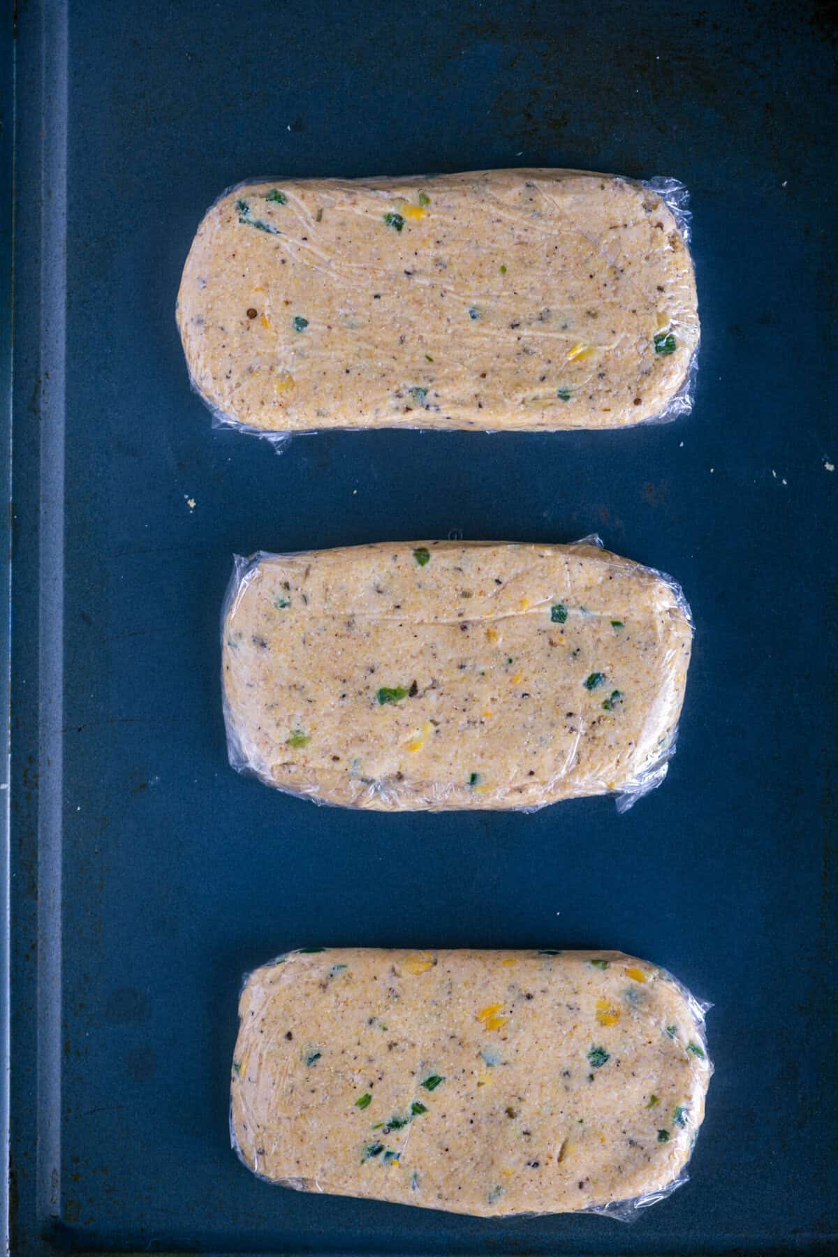 Flattened cornbread biscotti logs baked until firm on a lined baking tray.
