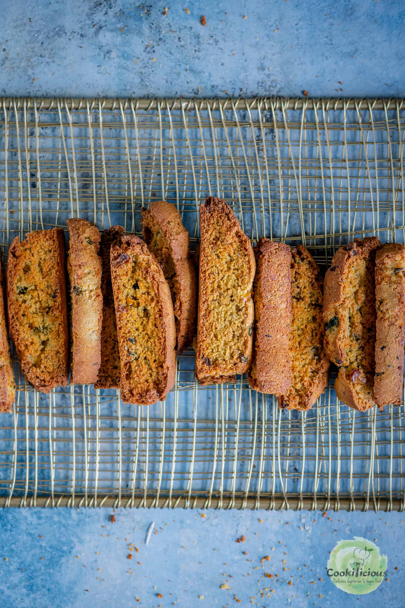 Crunchy jalapeño cheddar cornbread biscotti lined up on a gold wire cooling rack, showing flecks of sweet corn and jalapeño.