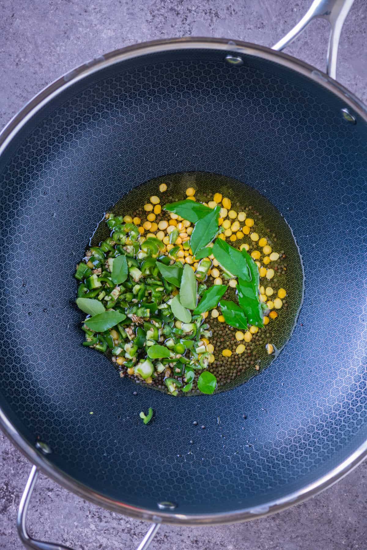 Mustard seeds, chana dal, chopped green chillies, and curry leaves tempering in oil in a wok for chivda.