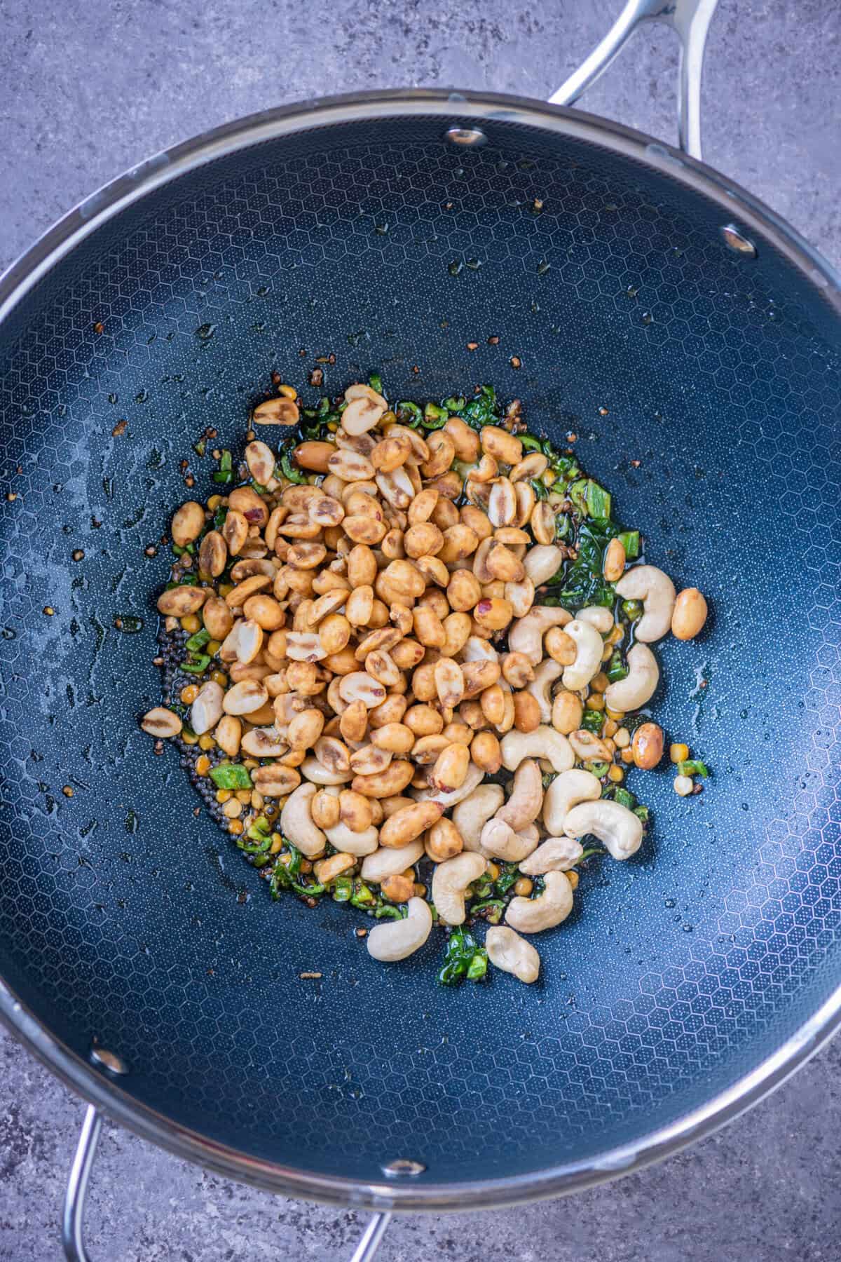Peanuts and cashews added to the tempering in a wok for Rice Krispies chivda.