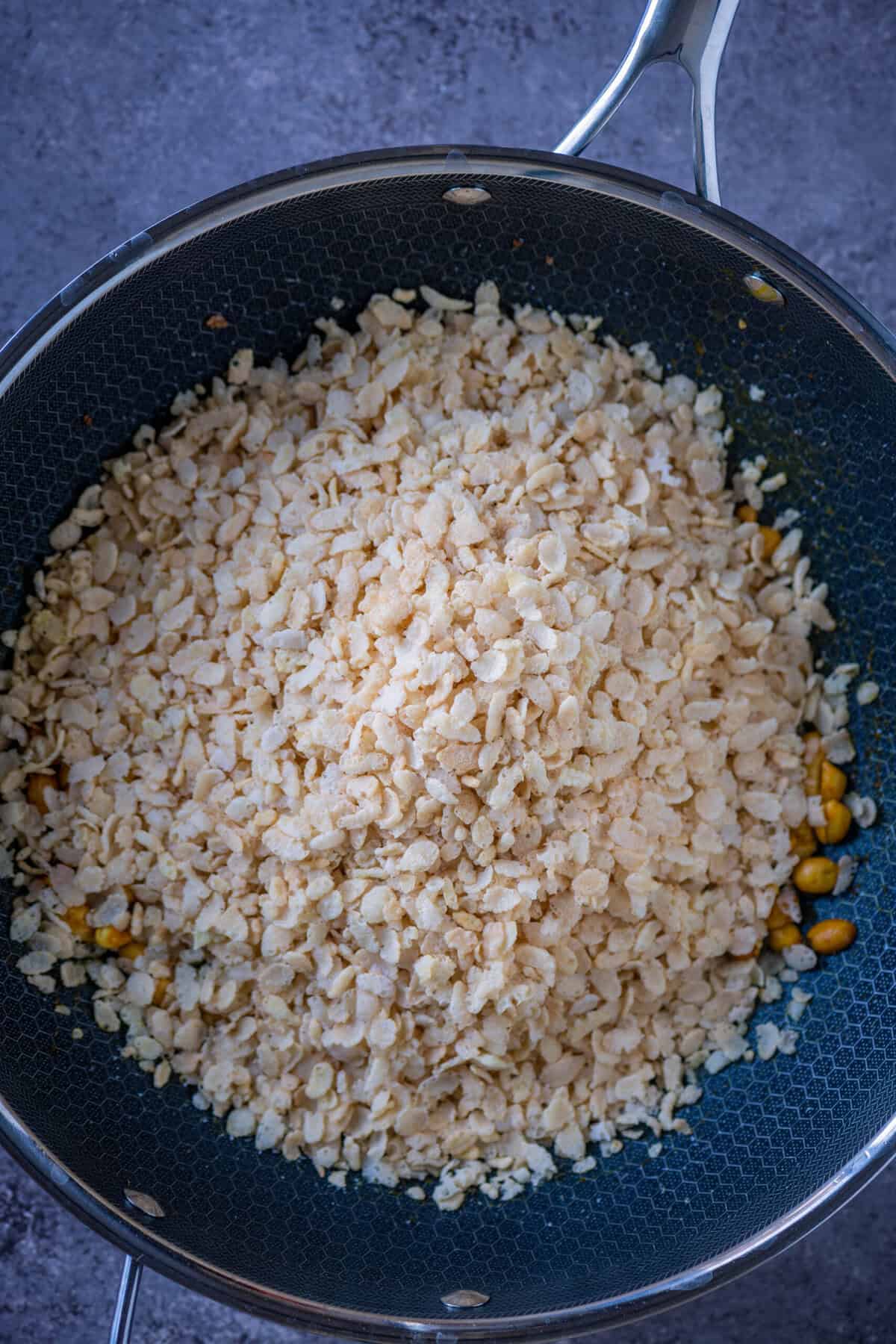 Rice Krispies cereal added to the spiced nuts in a wok to make namkeen chivda.