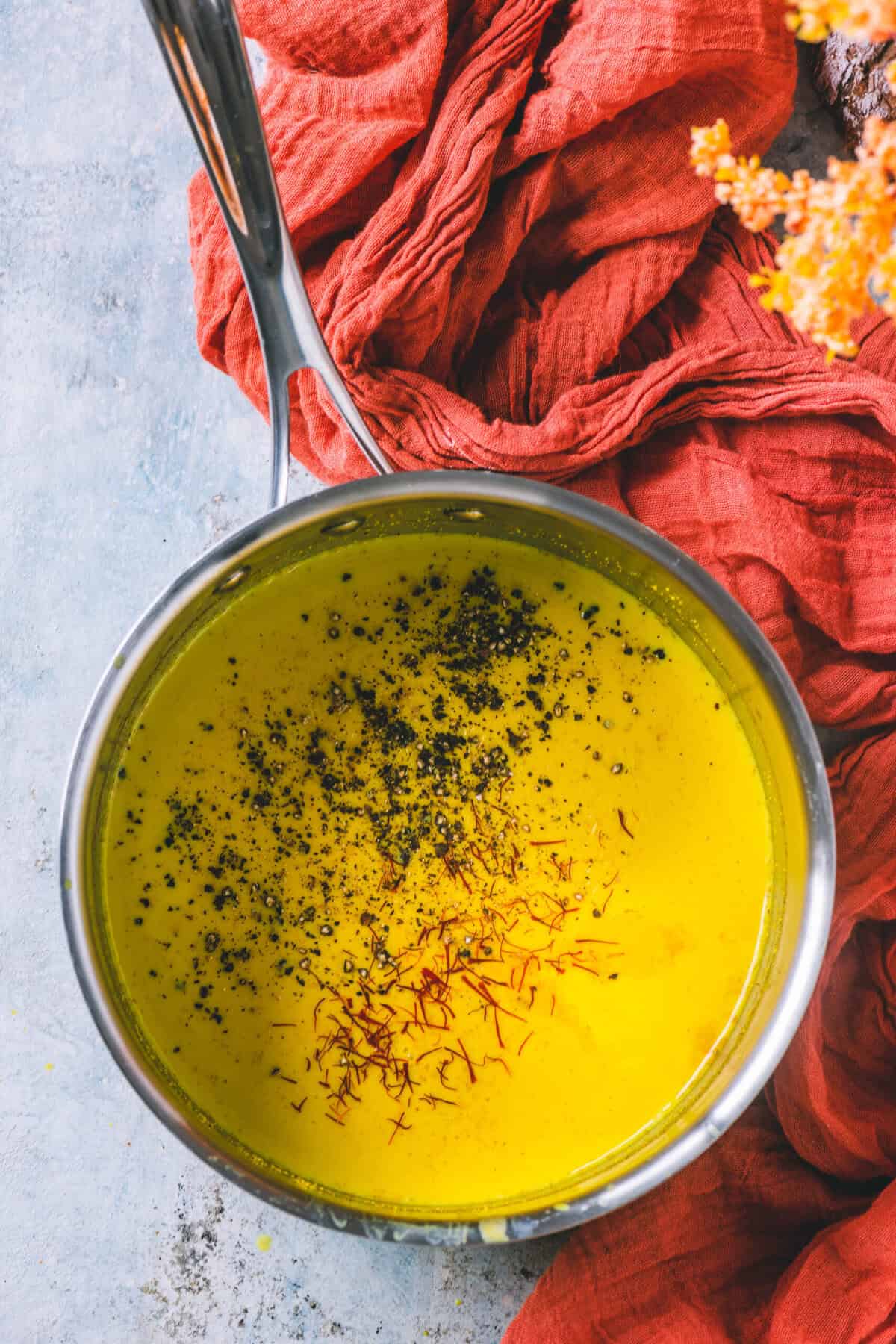 Golden milk in a glass topped with crushed black pepper and saffron strands.