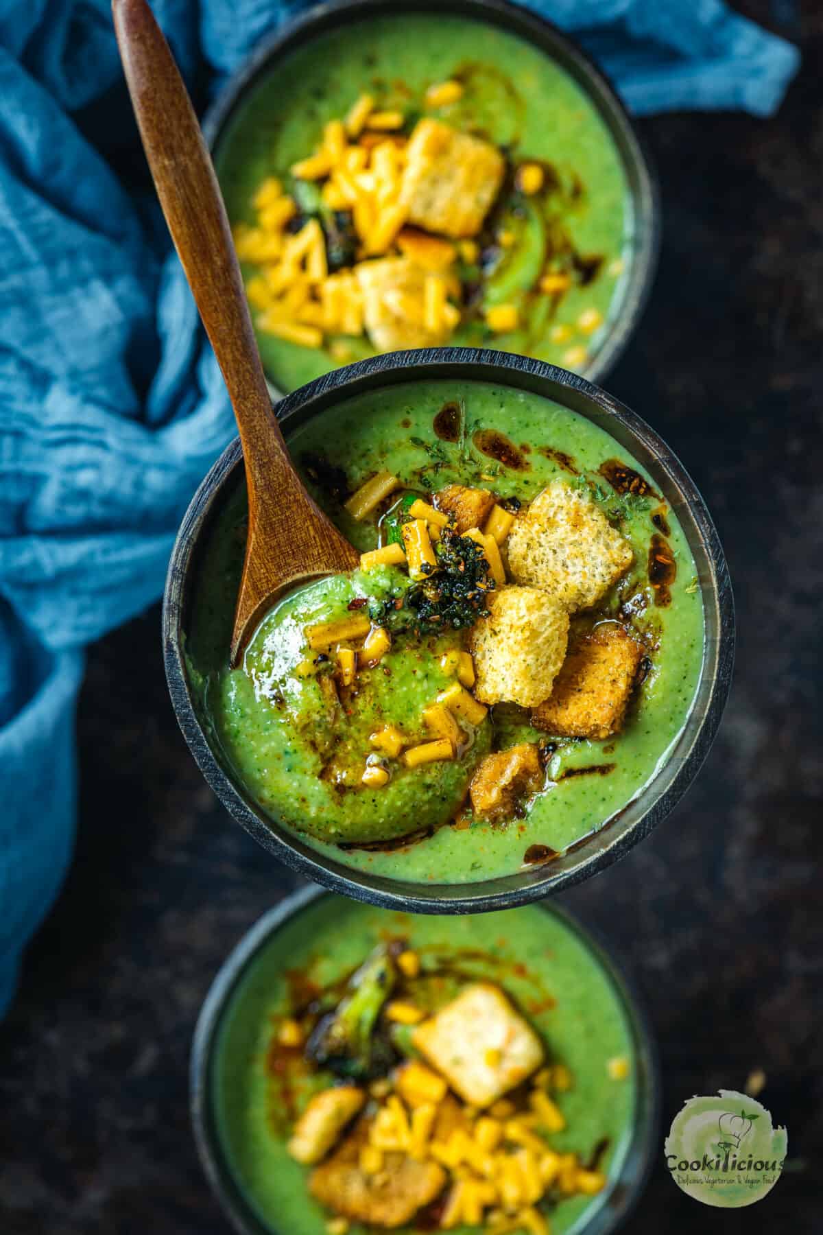 close up of Vegan Broccoli Cheddar Soup in a wooden bowl with a spoon in it.