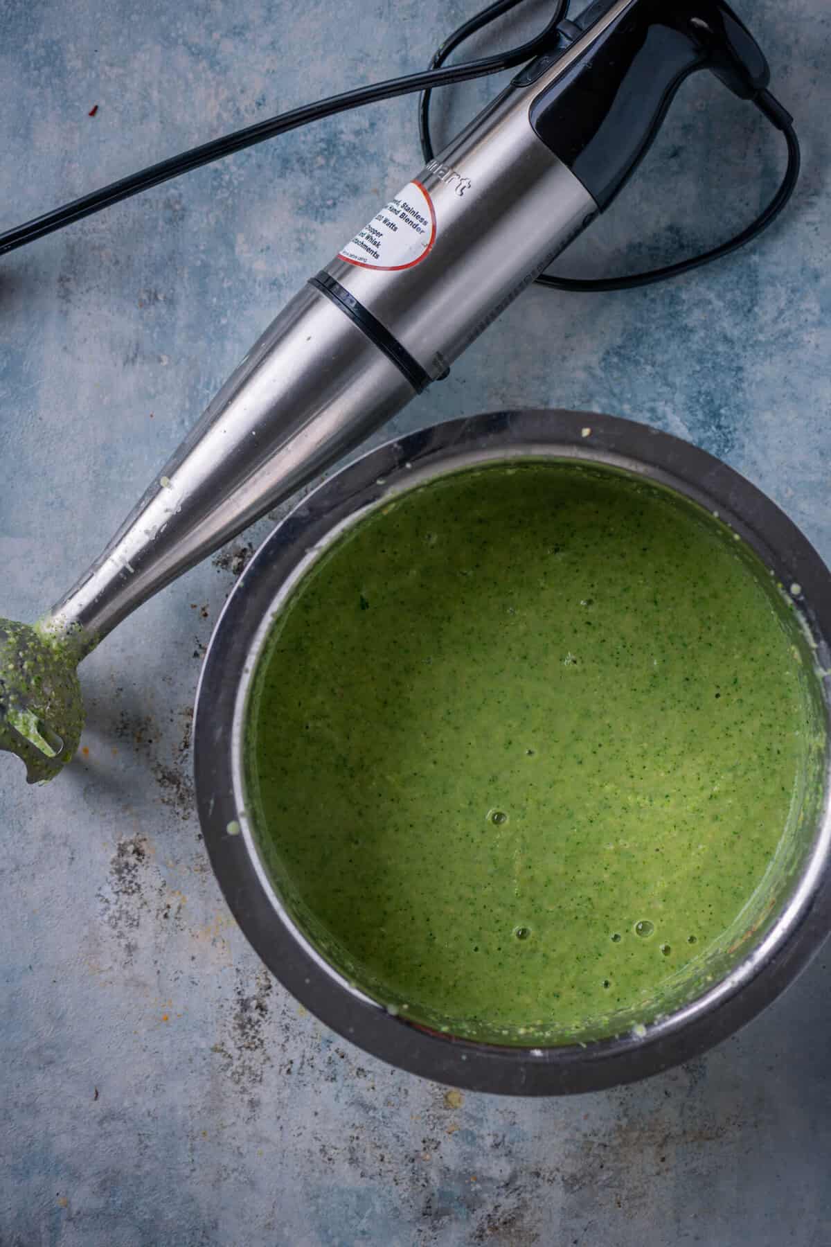 Blending broccoli soup into a smooth vegan puree with a hand blender.