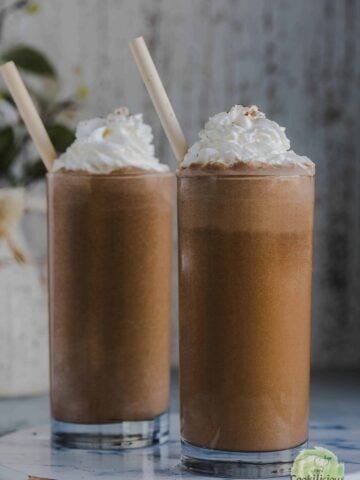 2 glasses of chikoo milkshake served with whipped cream on top.