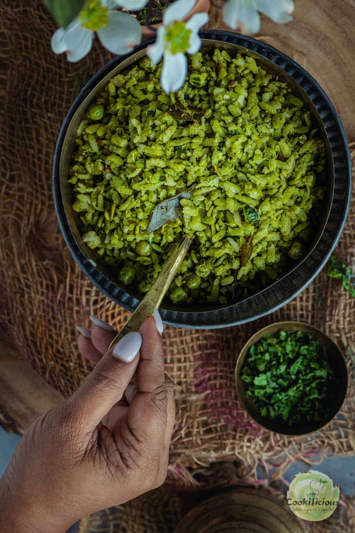 A hand digging into a bowl of Hariyali poha with a spoon.