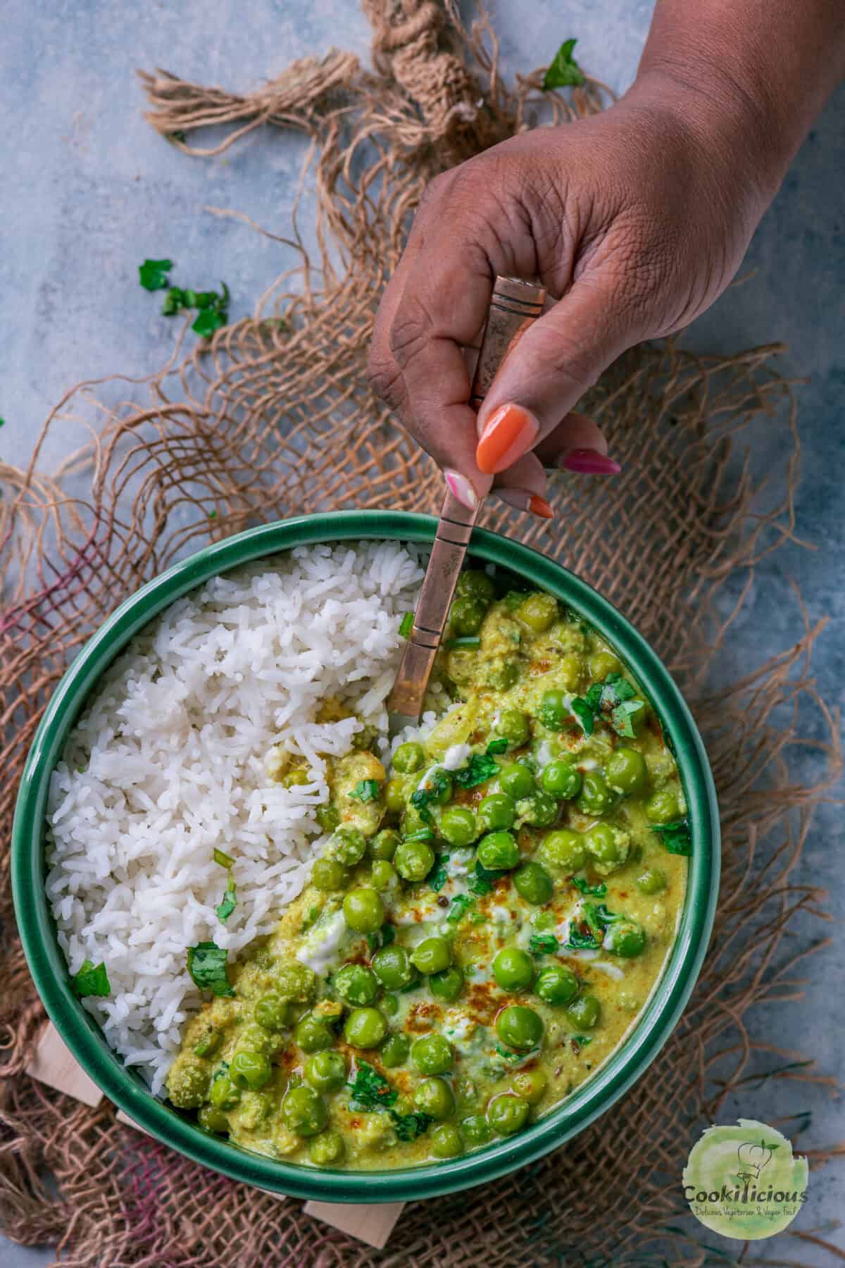 A hand holding a spoon and digging into a plate of Kovalam Matar and rice.