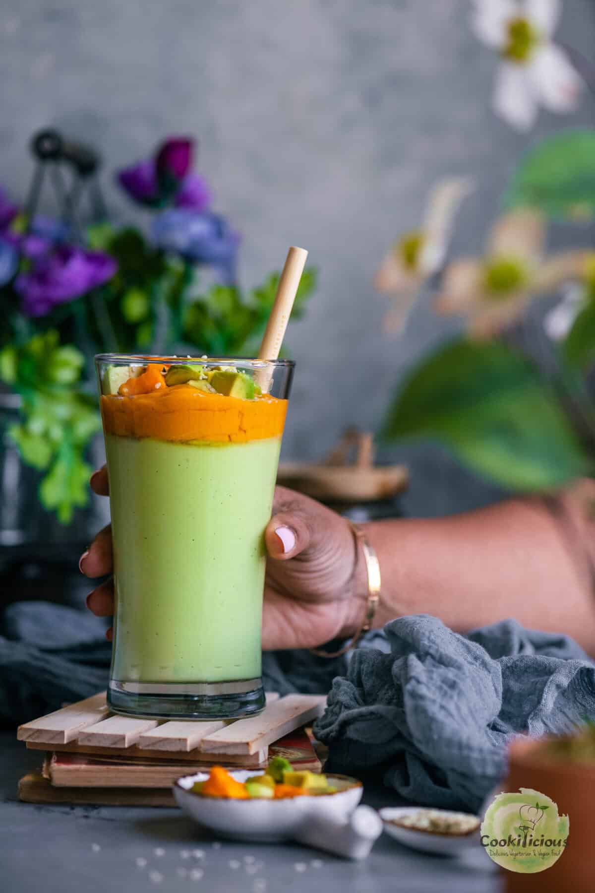 A hand holding a glass that's filled with avocado and mango smoothie.