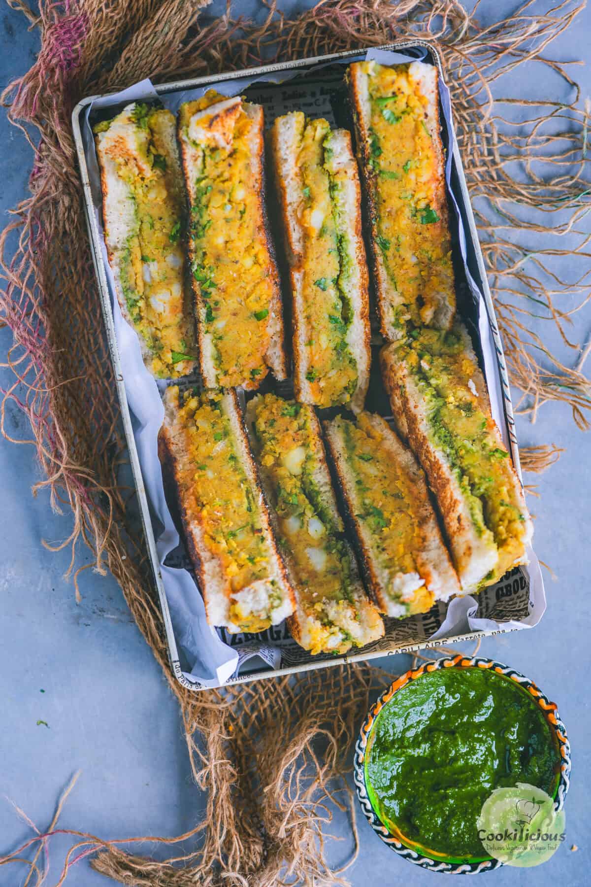 Aloo toast cut in triangles and served in a tray with green chutney on the side.
