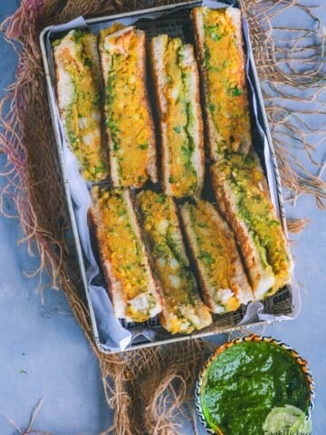 Aloo toast cut in triangles and served in a tray with green chutney on the side.
