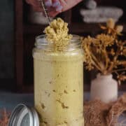 Scooping out homemade ginger paste from a jar using a spoon.