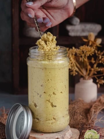 Scooping out homemade ginger paste from a jar using a spoon.