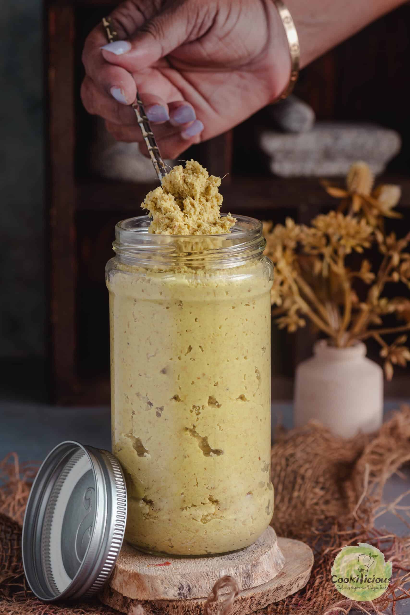 Scooping out homemade ginger paste from a jar using a spoon.