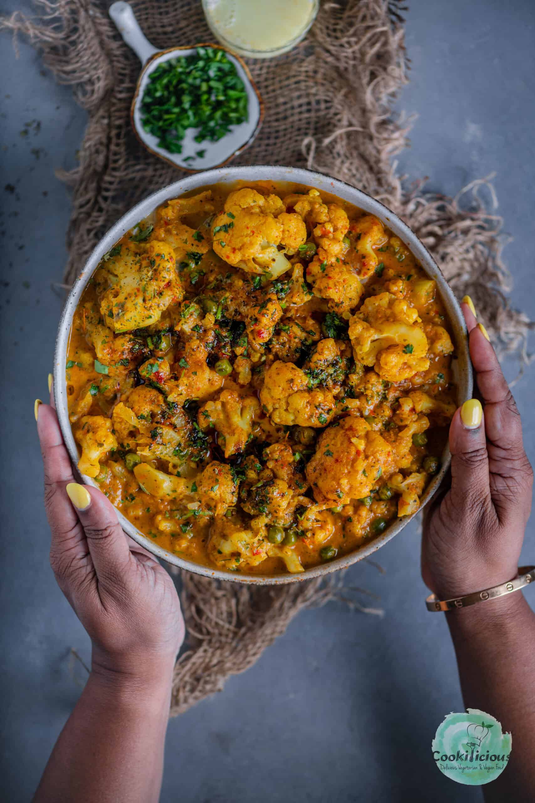 a set of hands holding a bowl of Indian Cauliflower Tikka Masala.