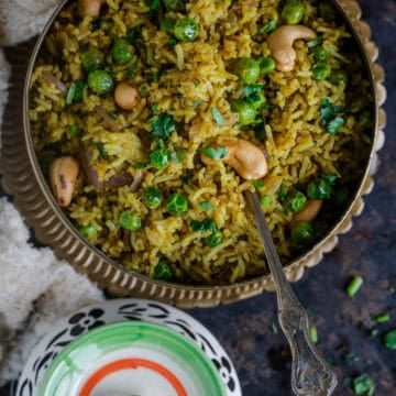 Matar pulao served in a round bowl with a spoon in it,