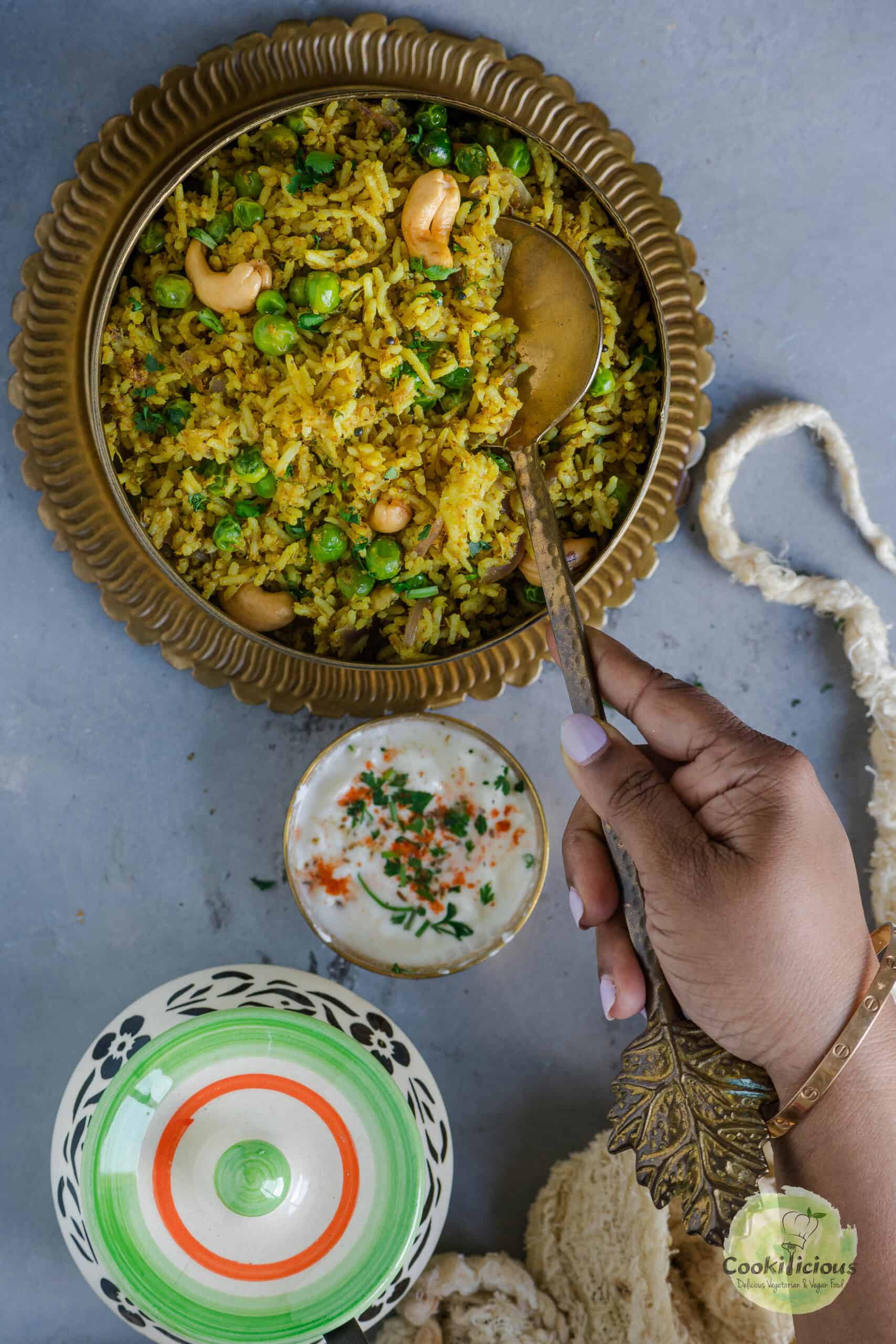 A hand digging into a bowl of green peas pulao holding a spoon.