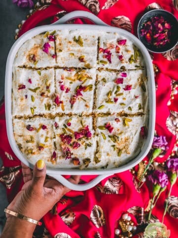 a hand holding a casserole of rasmalai cake.