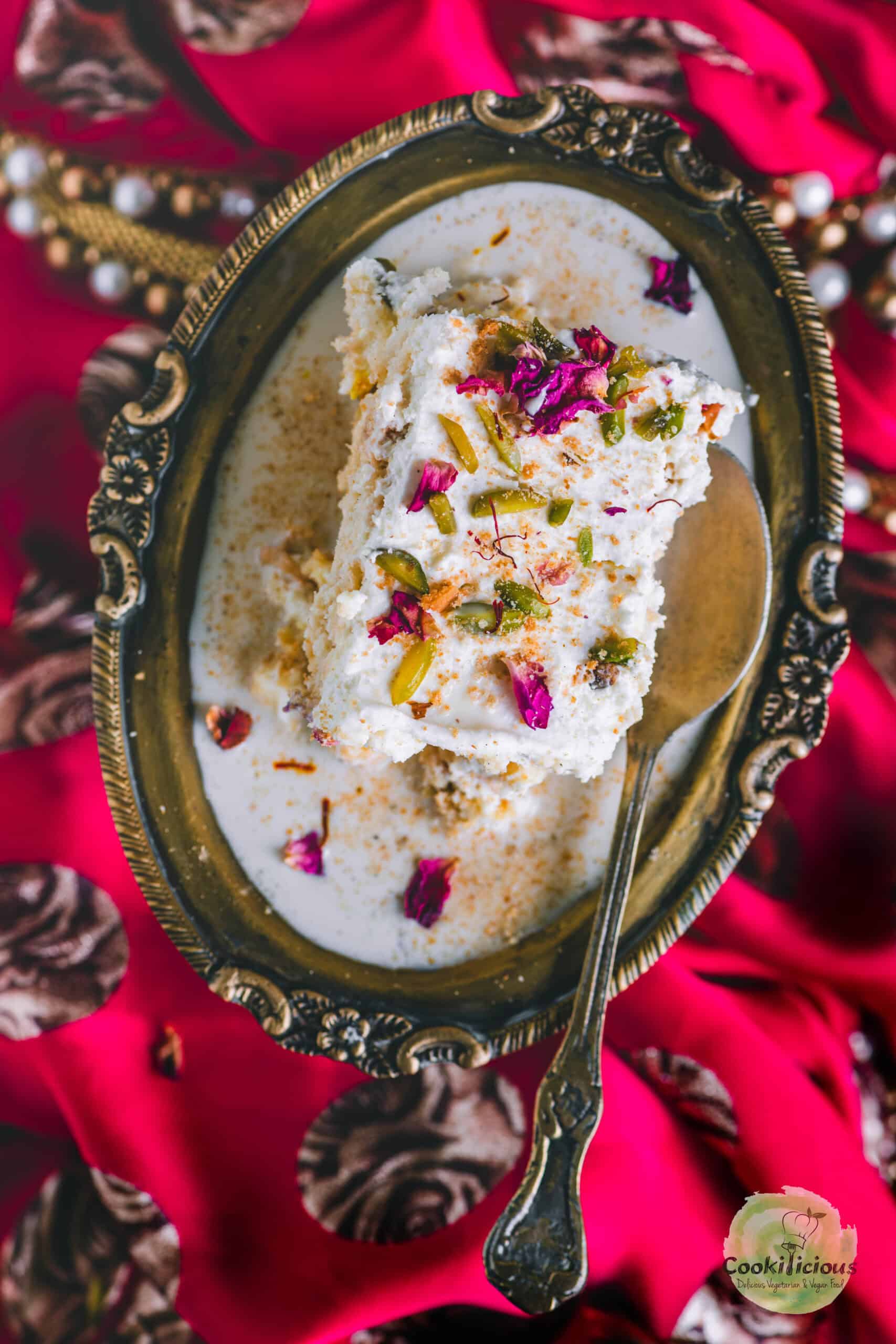 a slice of rasmalai cake served in an oval dish with a spoon in it.