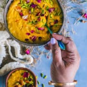 A hand digging into a bowl of Mango Phirni with a spoon.