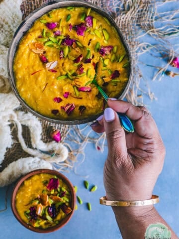 A hand digging into a bowl of Mango Phirni with a spoon.