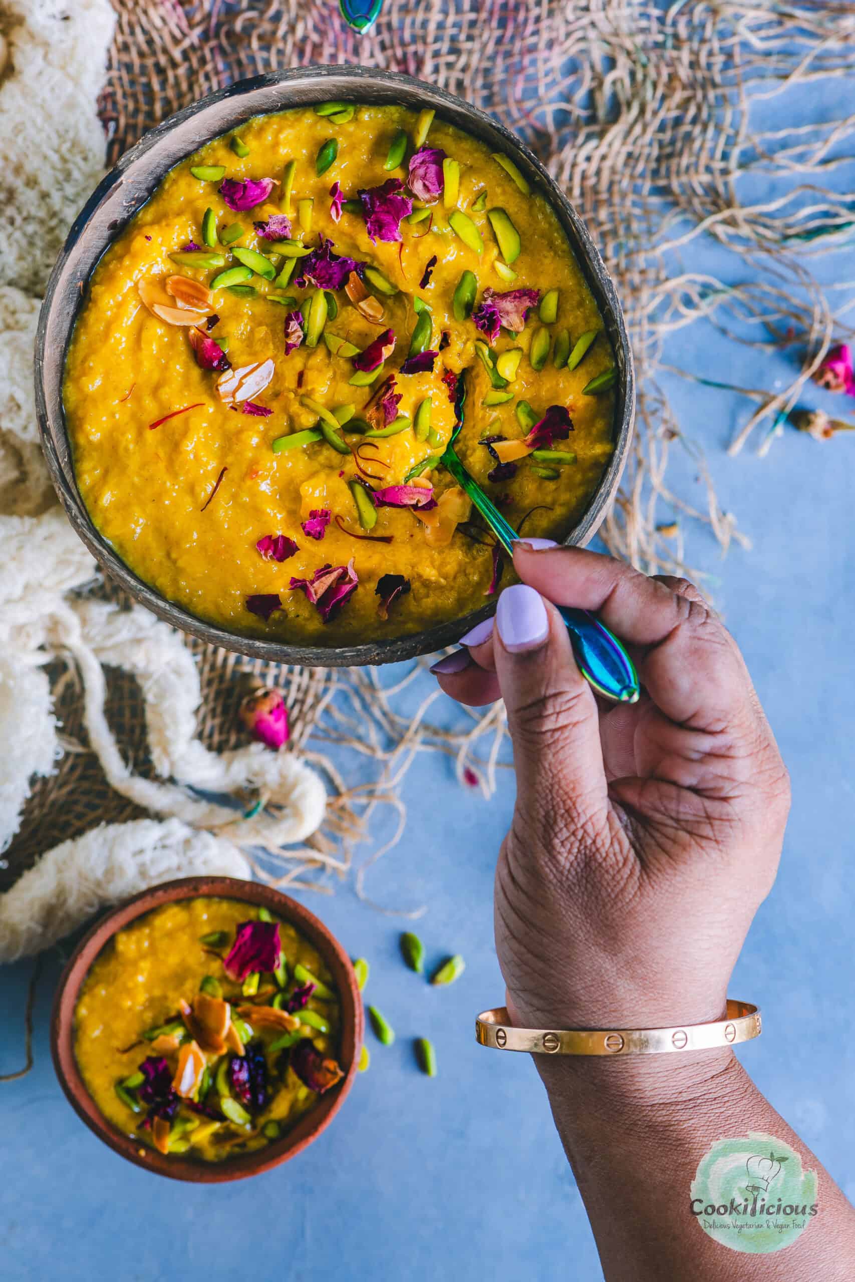 A hand digging into a bowl of Mango Phirni with a spoon.