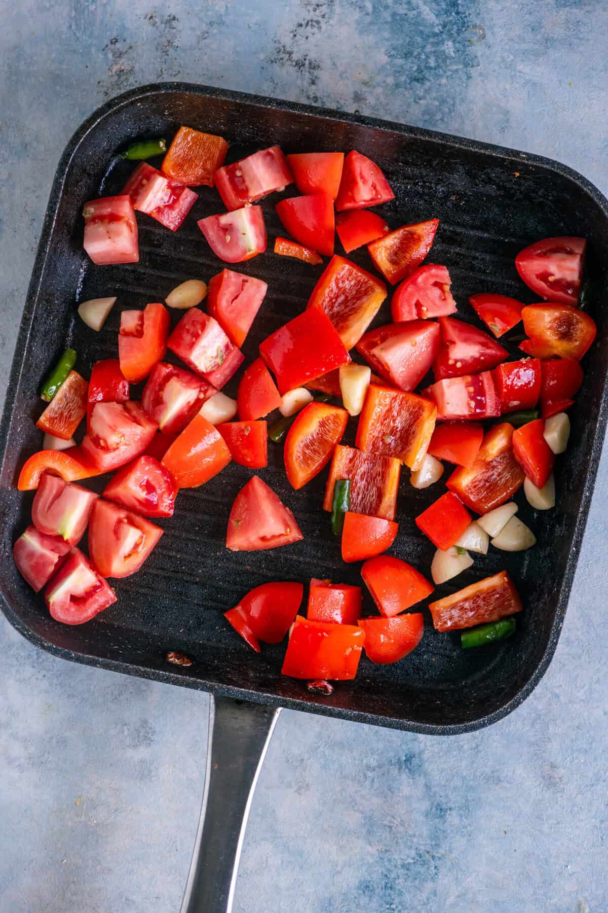 Bell peppers, tomatoes, garlic, and green chilies grilling in a pan for Indian kofta curry.